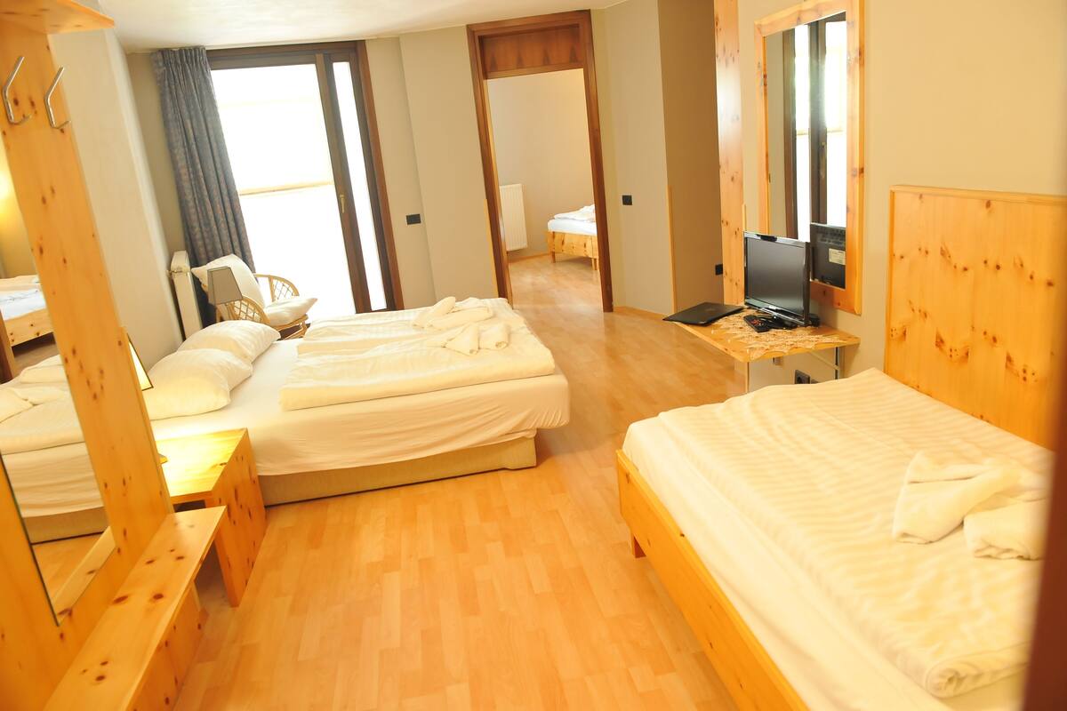 A hotel room with two beds, a wooden floor, a desk with a laptop, and a TV.