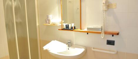 A bathroom with a glass shower enclosure, a white sink with a mirror above it, and a telephone mounted on the wall.