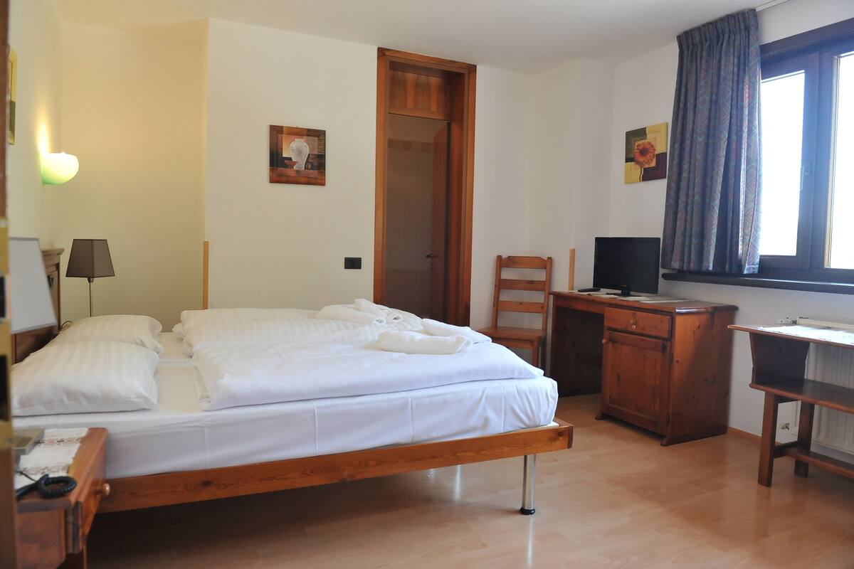 A bedroom with a wooden bed, a desk, a chair, and a television.