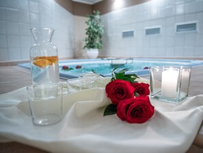A spa area with a pool, a glass bottle with a slice of orange, and three red roses on a white cloth. - Al Gallo Forcello 1530 (Pontebba)