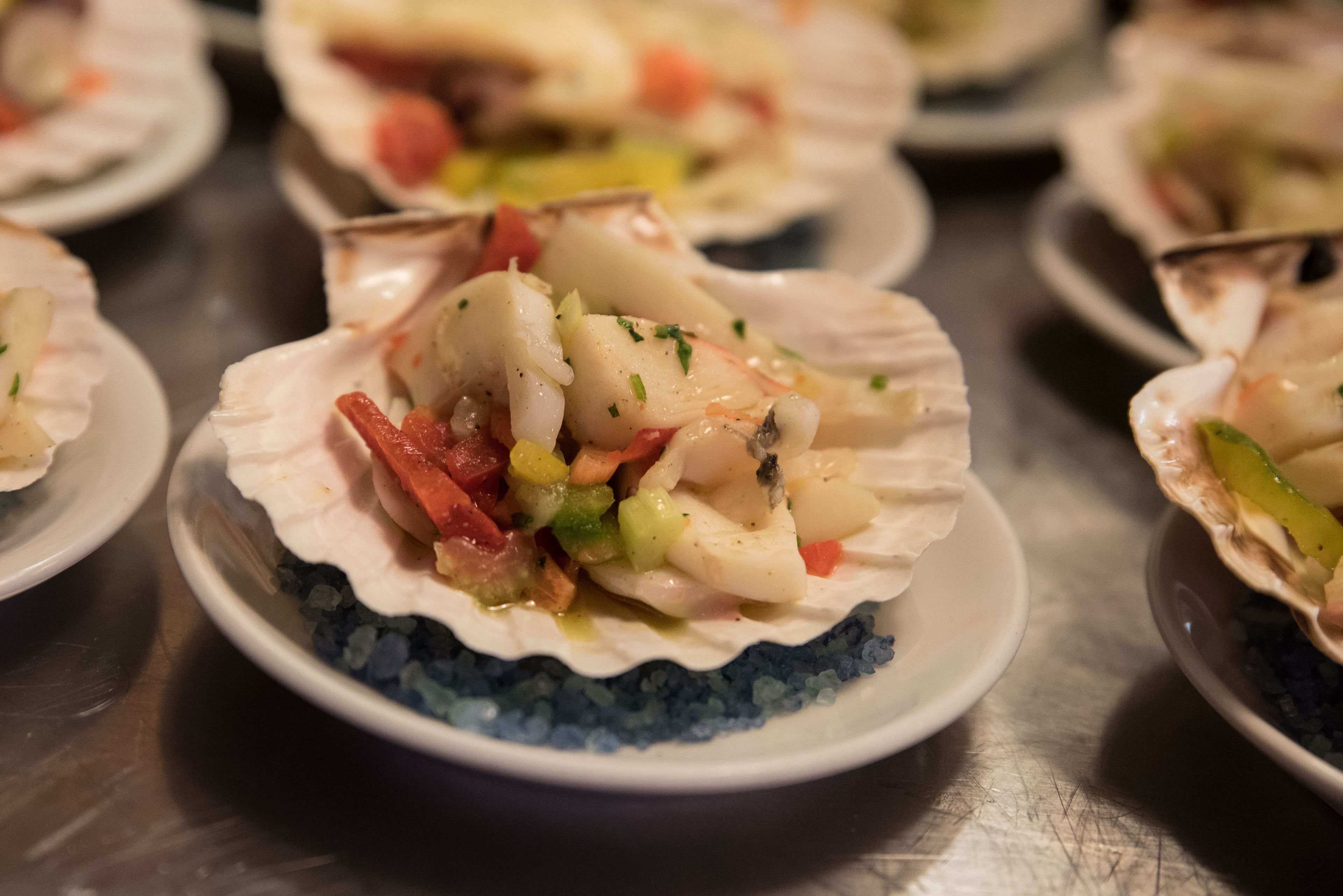 A seafood dish served in a scallop shell on a plate with a blue rim.