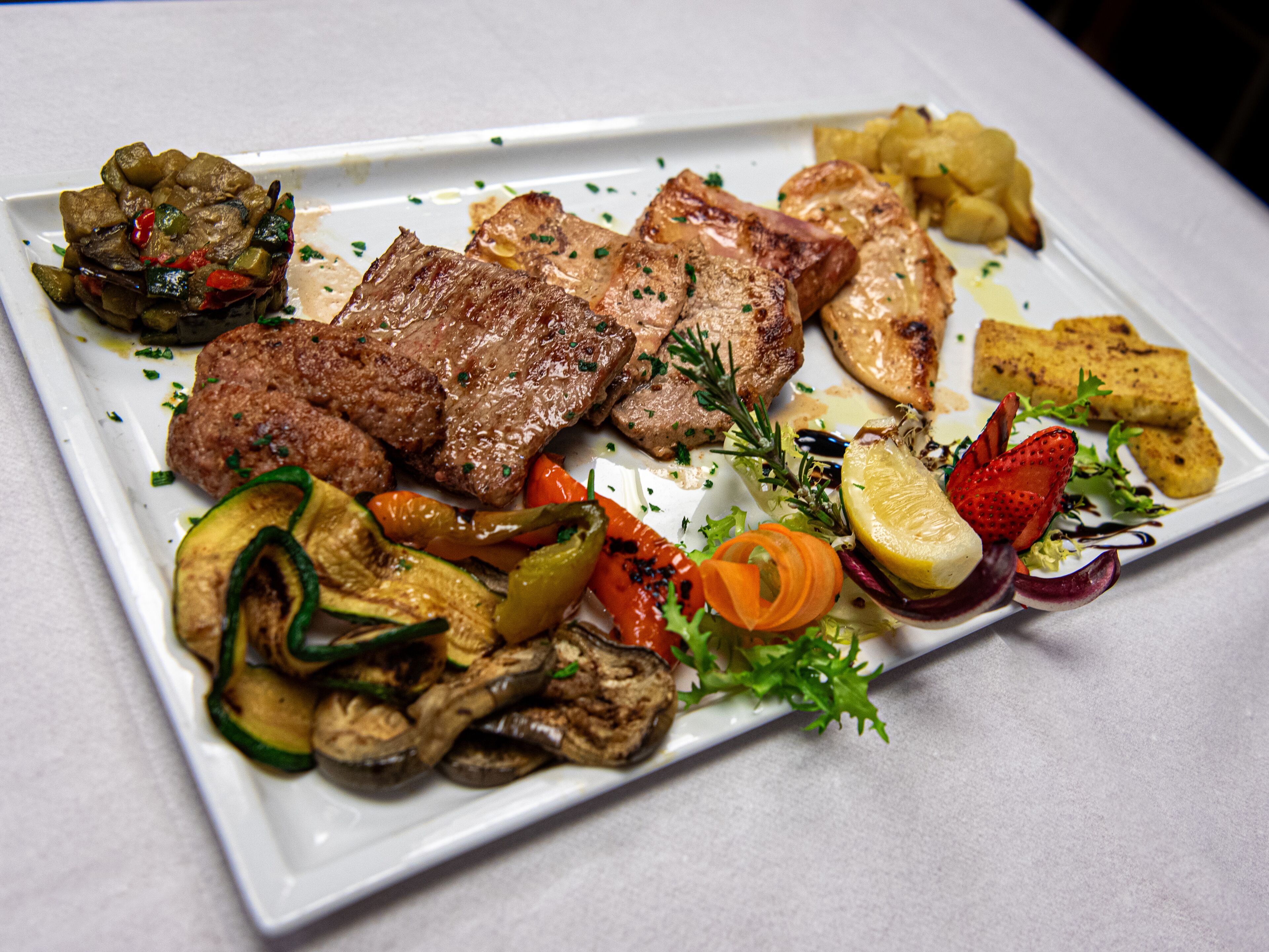 A plate of grilled steak with vegetables and a side of roasted potatoes.