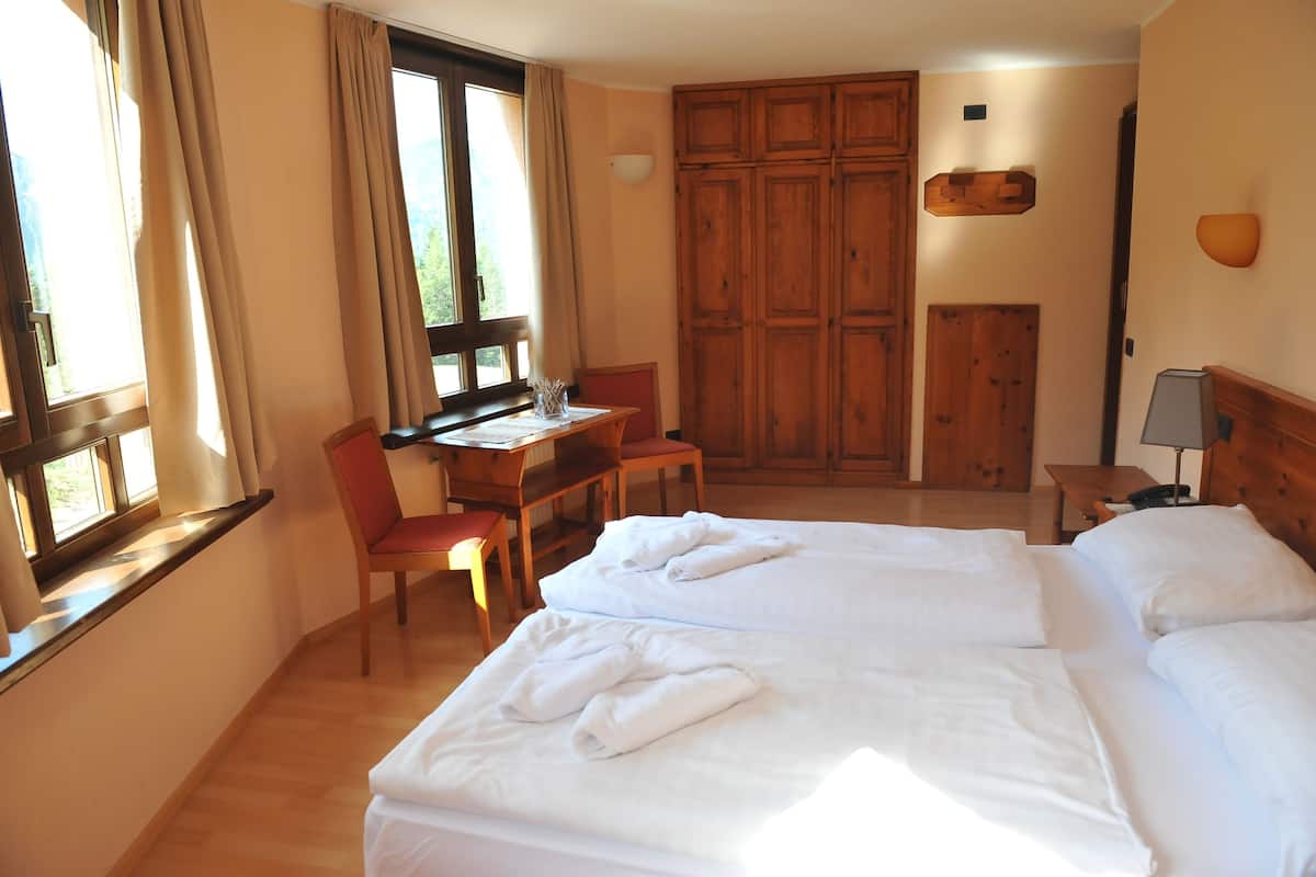 A hotel room with two beds, a desk, a chair, and a wardrobe.