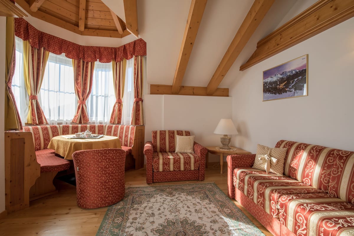 Una habitación acogedora con techo de madera, una mesa de comedor con sillas, un sofá y una alfombra estampada.