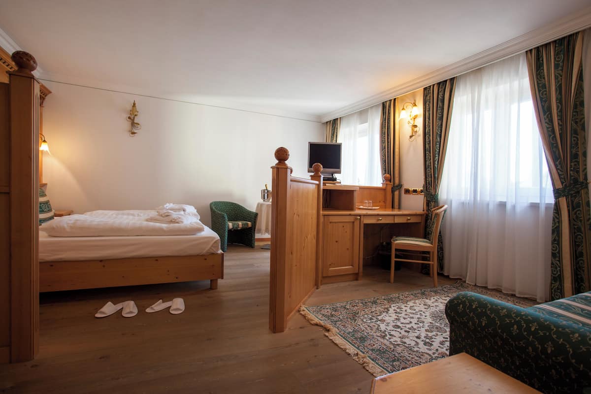 A hotel room with a wooden bed, a desk with a computer, a green armchair, and a patterned rug.
