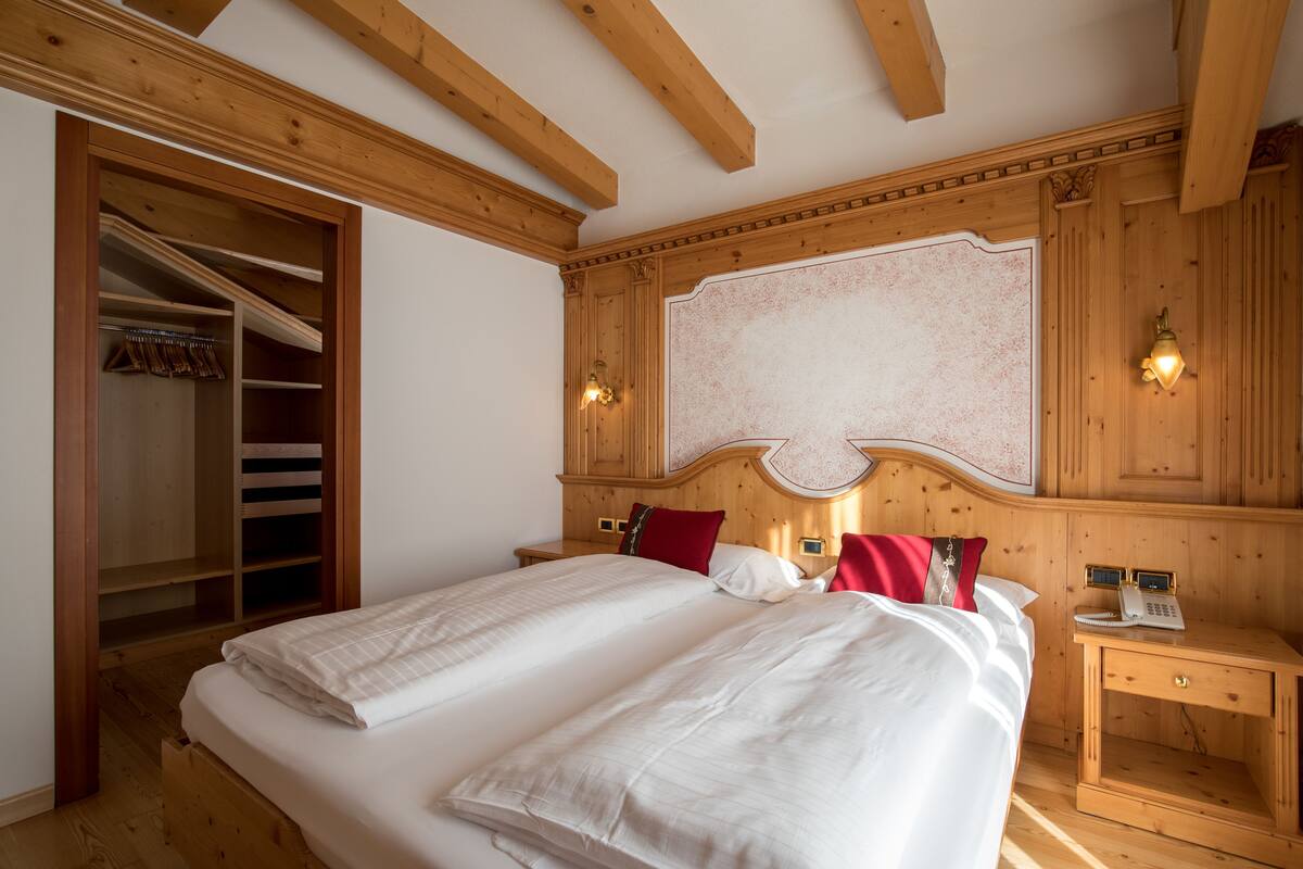 A bedroom with a large bed, wooden headboard, a built-in wardrobe, and a bedside table with a phone.