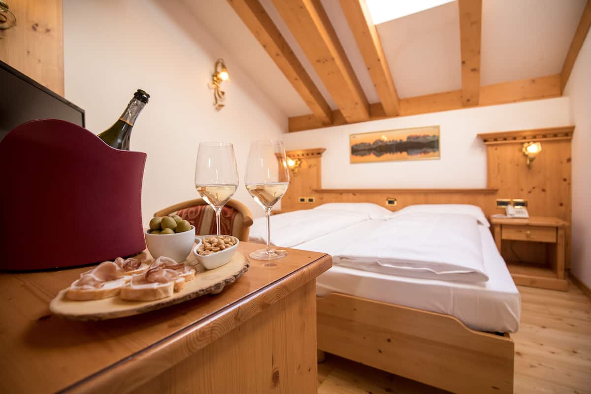 Una cama de madera con ropa de cama blanca, una mesita de noche con una botella de champán, dos copas, un cuenco de aceitunas y un plato de carne cortada.