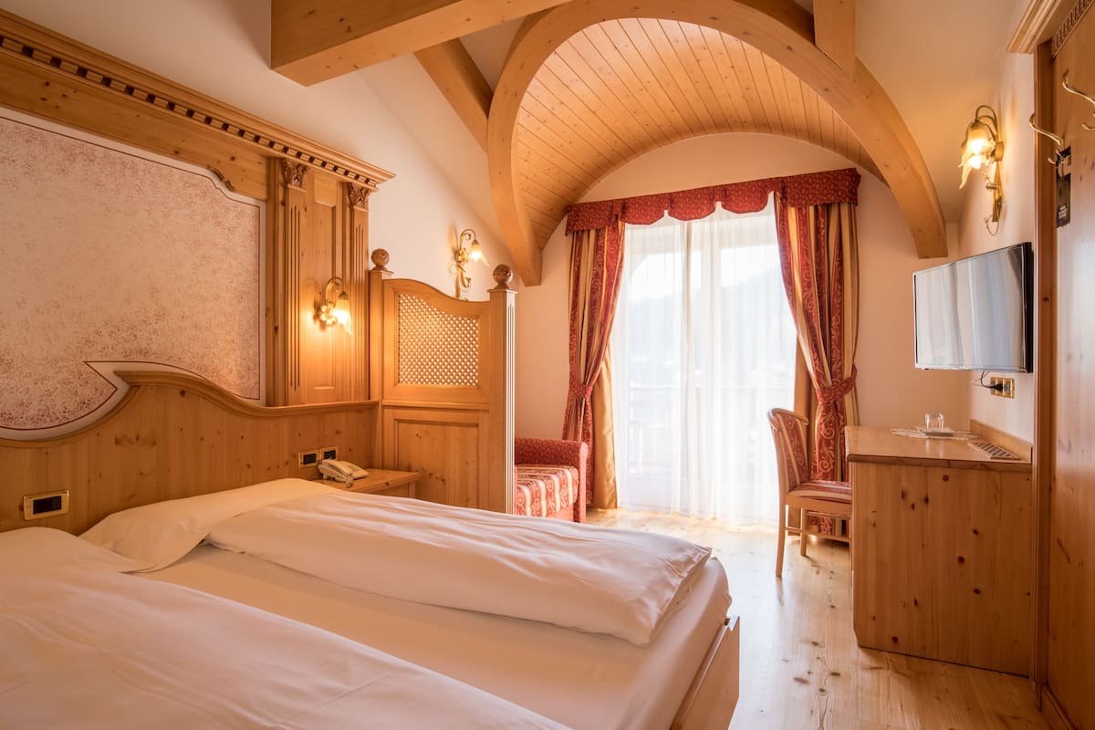 Habitación de hotel con una cama grande, cabecera de madera, un escritorio con silla, televisión y ventana con cortinas.