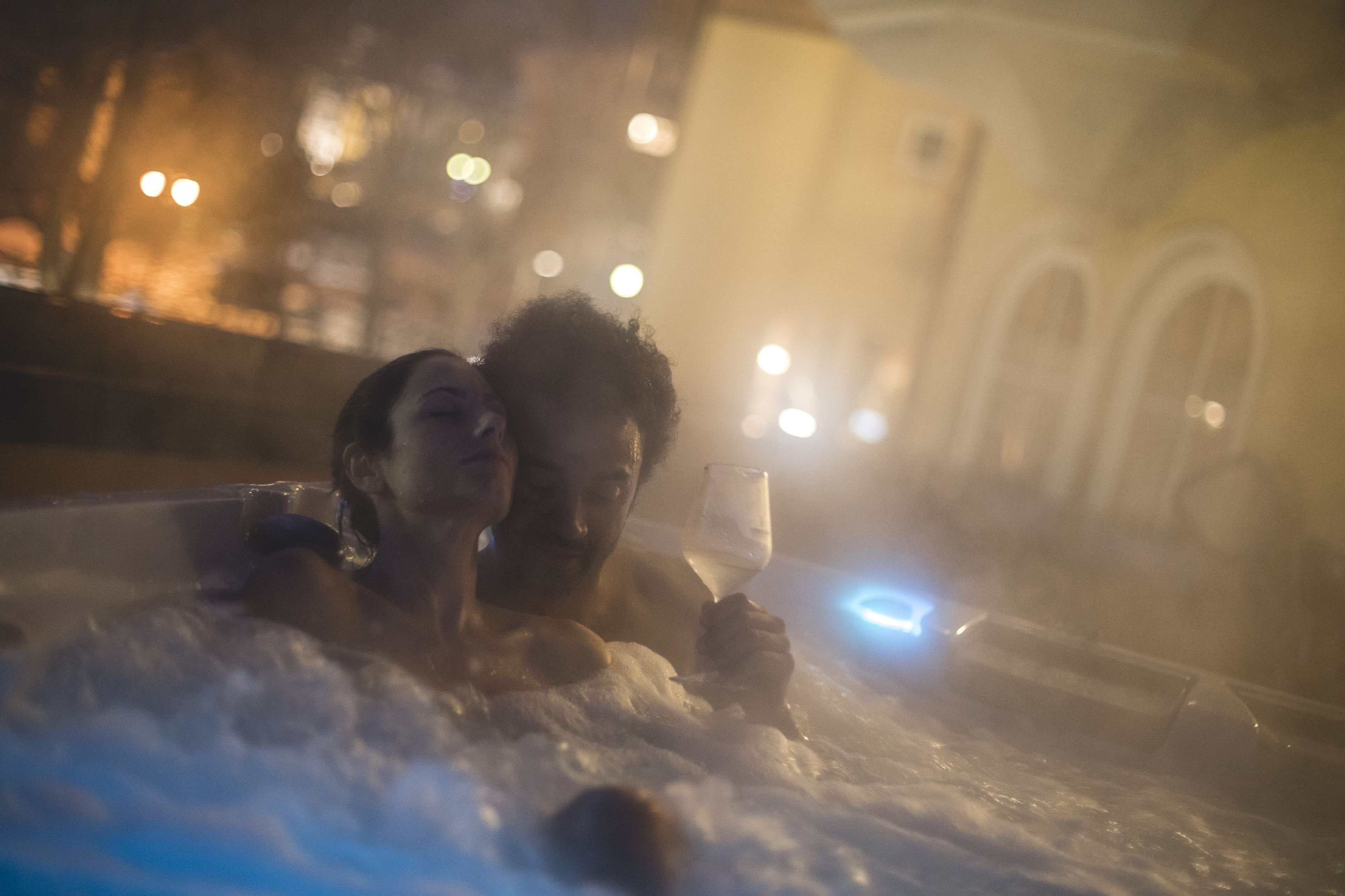 A couple in a hot tub with a cityscape in the background.