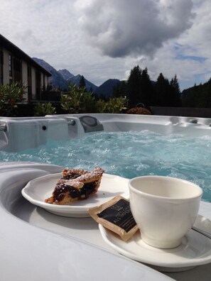 A hot tub with a slice of pie and a cup on a tray, set against a backdrop of mountains and trees. - Hotel Chalet all'Imperatore (Tre Ville)