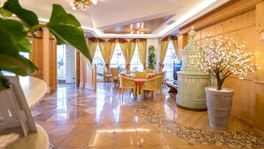 A lobby with a wooden reception desk, a dining area with yellow chairs, and a large potted tree with white blossoms. - Hotel Chalet all'Imperatore (Tre Ville)