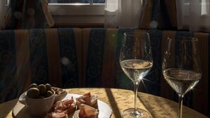 A table with a plate of food and two wine glasses, a window with curtains, and a view of mountains. - Hotel Chalet all'Imperatore (Tre Ville)