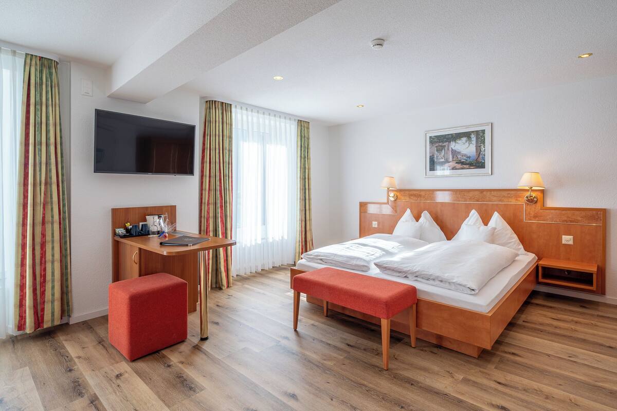 A hotel room with a wooden bed, a desk, a television, and a painting on the wall.