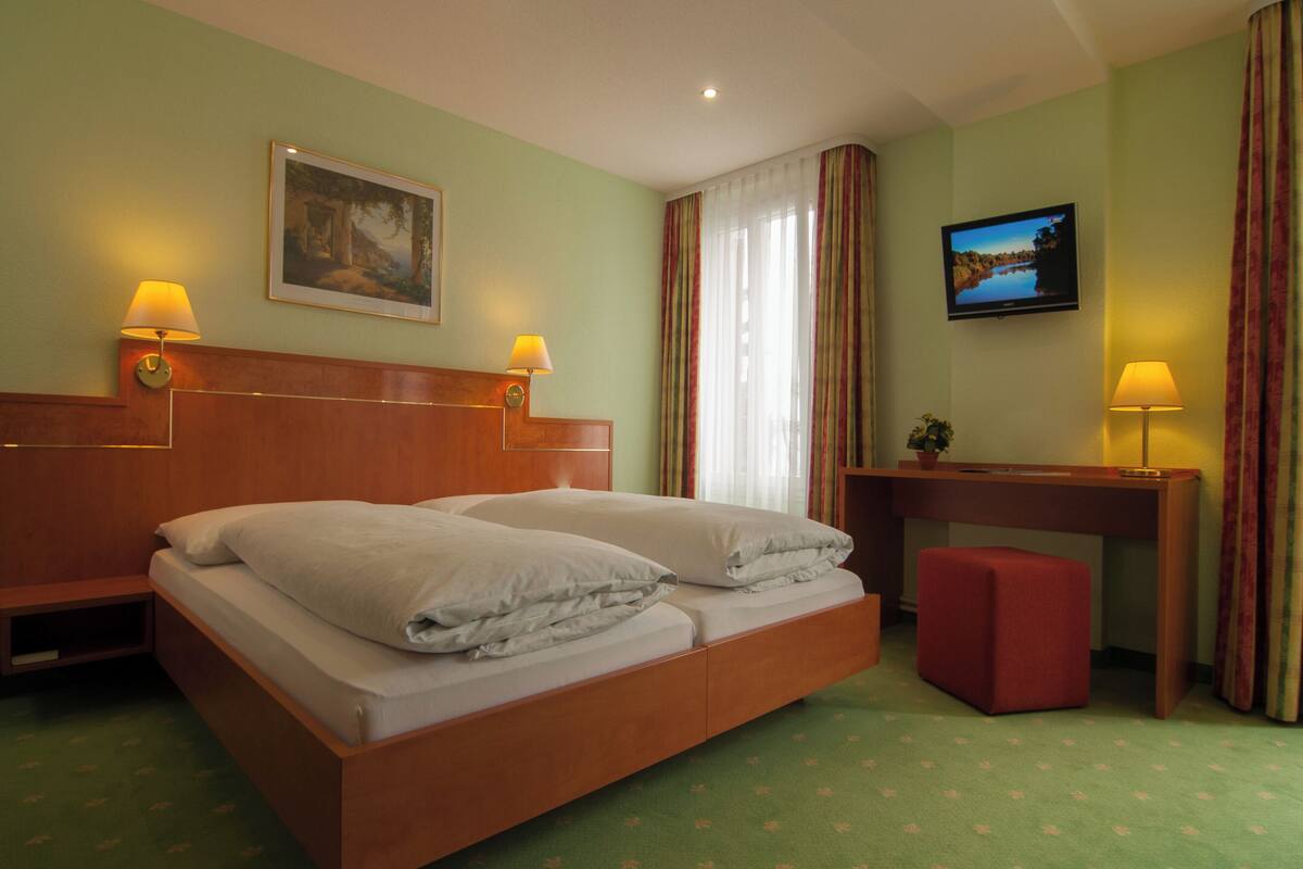 A hotel room with a wooden bed, two bedside lamps, a television, and a small desk with a chair.