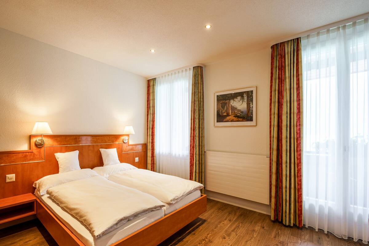 A hotel room with a double bed, wooden headboard, two bedside lamps, a framed picture on the wall, and striped curtains.