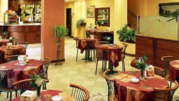 A hotel dining area with multiple tables and chairs, a bar area, and a staircase leading to an upper level. - Hotel York (Cinisello Balsamo)