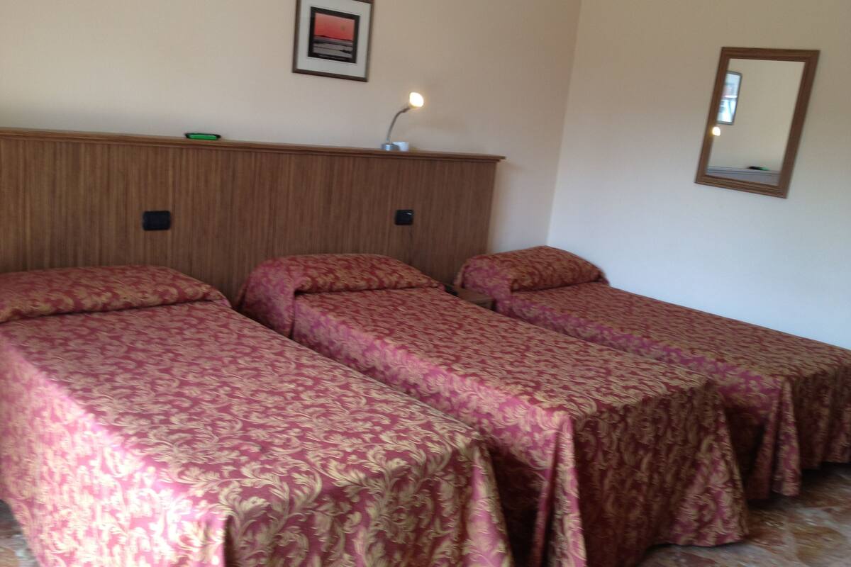 A room with two single beds, a wooden headboard, a framed picture on the wall, and a bedside lamp.