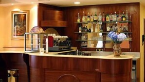 A bar area with wooden cabinetry, a countertop, and a variety of liquor bottles. - Hotel York (Cinisello Balsamo)
