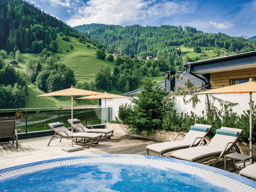 A rooftop pool area with lounge chairs and umbrellas, overlooking a mountainous landscape.