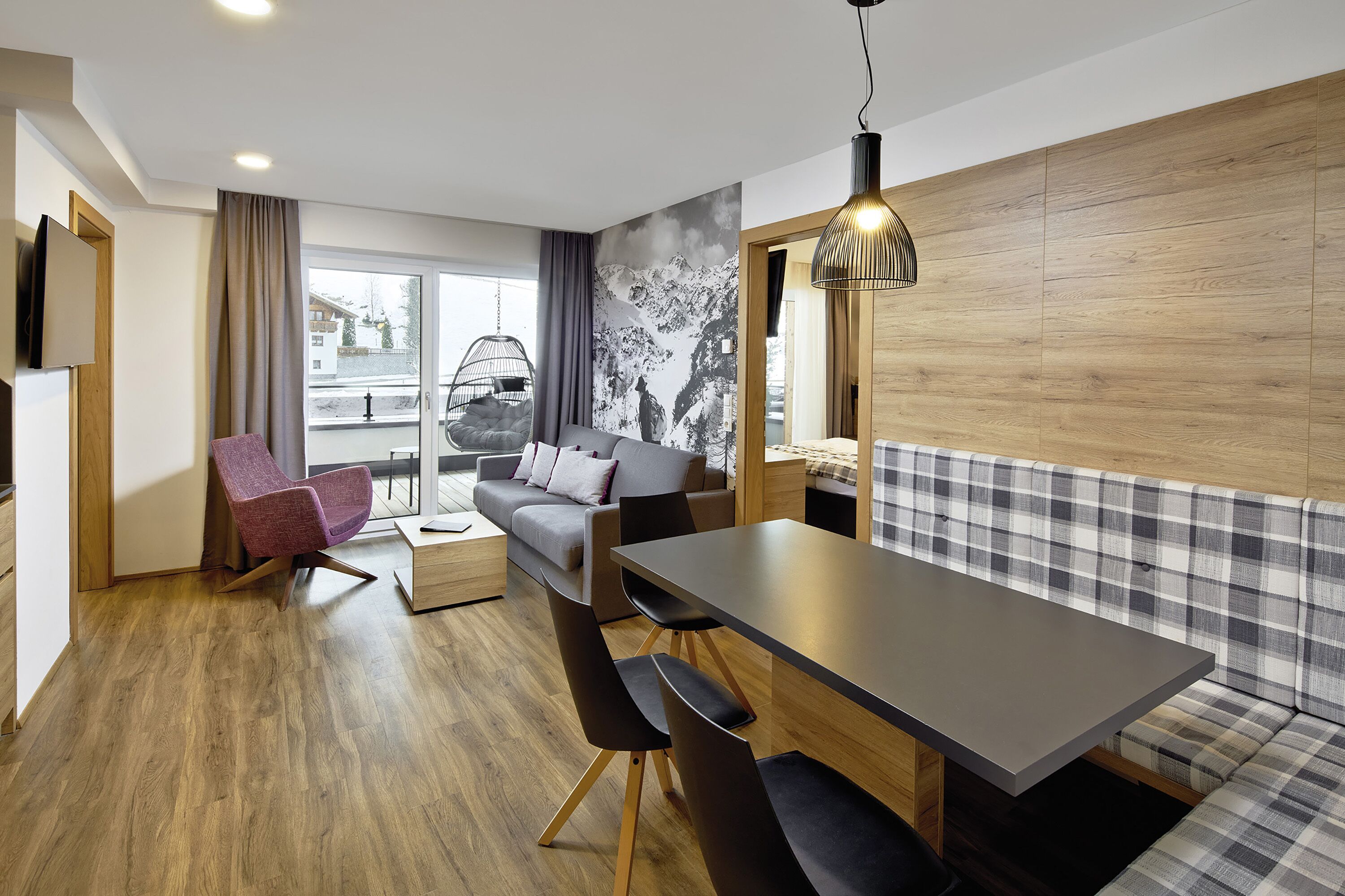 Een moderne, goed verlichte kamer met houten vloer, een bank, een eettafel en een hangstoel.