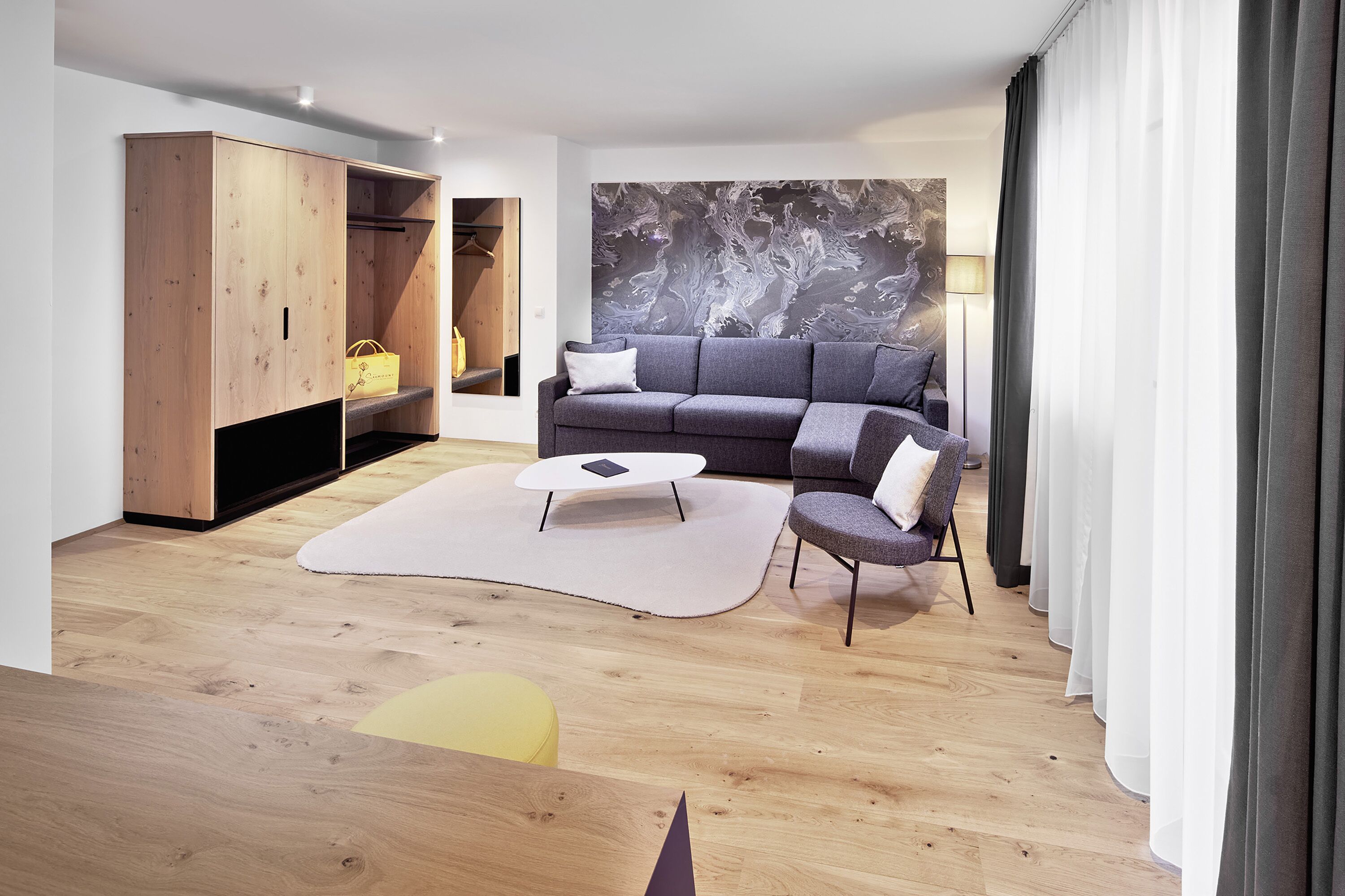 A modern living room with a grey sofa, a wooden wardrobe, a white coffee table, and a large abstract painting on the wall.