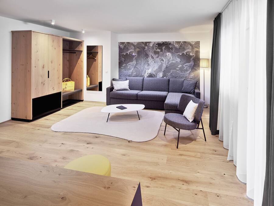 A modern living room with a grey sofa, a wooden wardrobe, a white coffee table, and a large abstract painting on the wall.