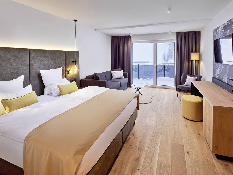 A modern hotel room with a large bed, a sofa, a desk, and a TV.