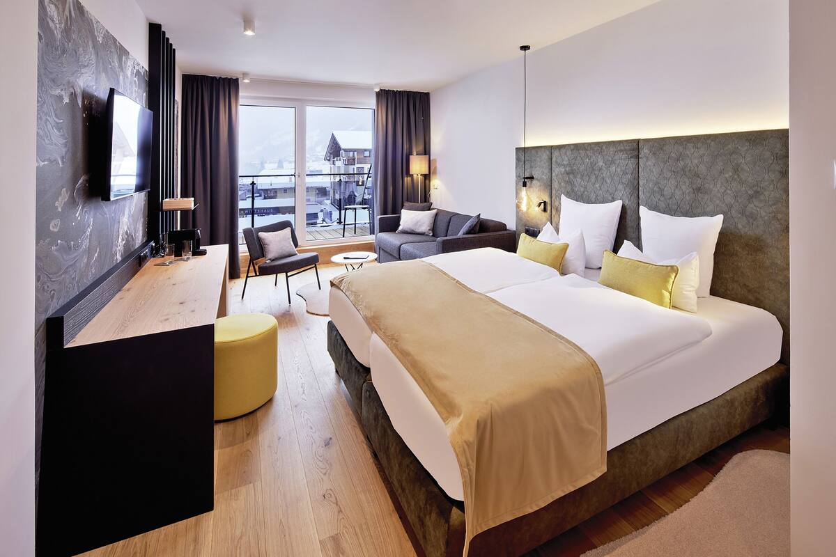 A modern hotel room with a large bed, a sofa, a desk, and a TV.