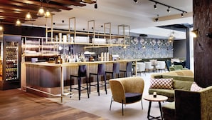 Eine moderne Bar mit Holzboden, Barhocker, einer Theke inklusive Weinkühler und einer Sitzecke mit Sofas und einem runden Tisch.