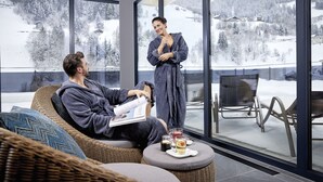 Ein modernes Interieur mit einem großen Fenster mit Blick auf eine verschneite Landschaft, einem Korbssessel und einem kleinen Tisch mit Getränken.