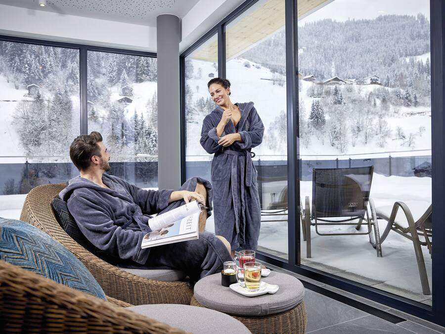 Un intérieur moderne avec une grande fenêtre donnant sur un paysage enneigé, un canapé en osier et une petite table avec des boissons.