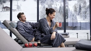 Ein Paar in einem gemütlichen, modernen Zimmer mit einem großen Fenster mit Blick auf eine verschneite Landschaft.