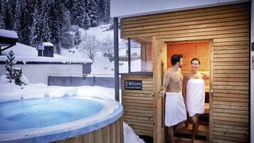 A wooden sauna with a sign indicating a height of 80 cm, a hot tub, and a snowy outdoor setting.
