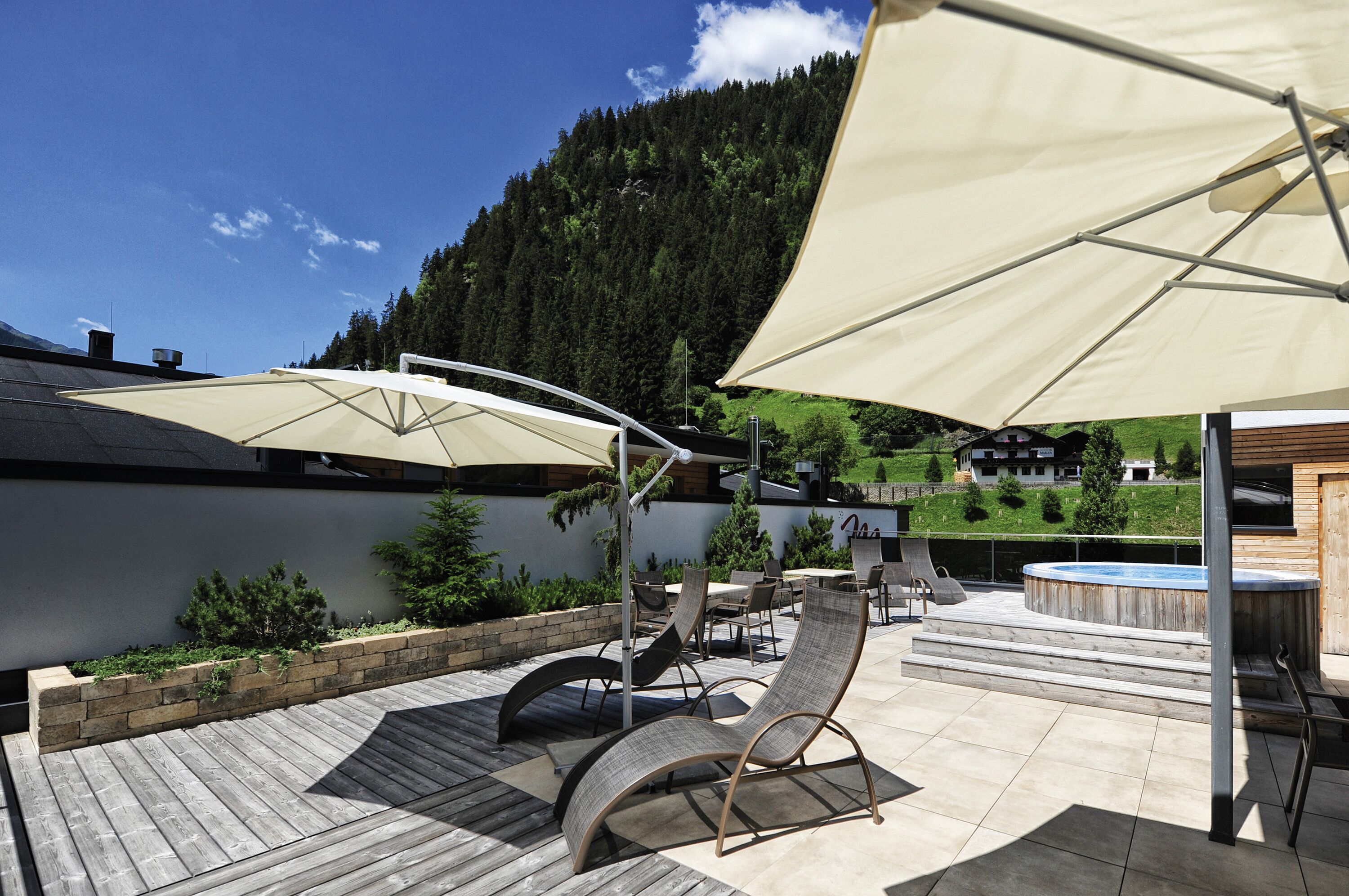 A patio with outdoor furniture, a hot tub, and a view of a forested mountain.