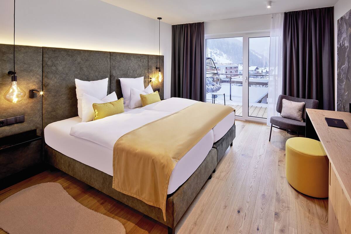 A modern hotel room with a large bed, a wooden desk, a chair, and a view of a snowy landscape.