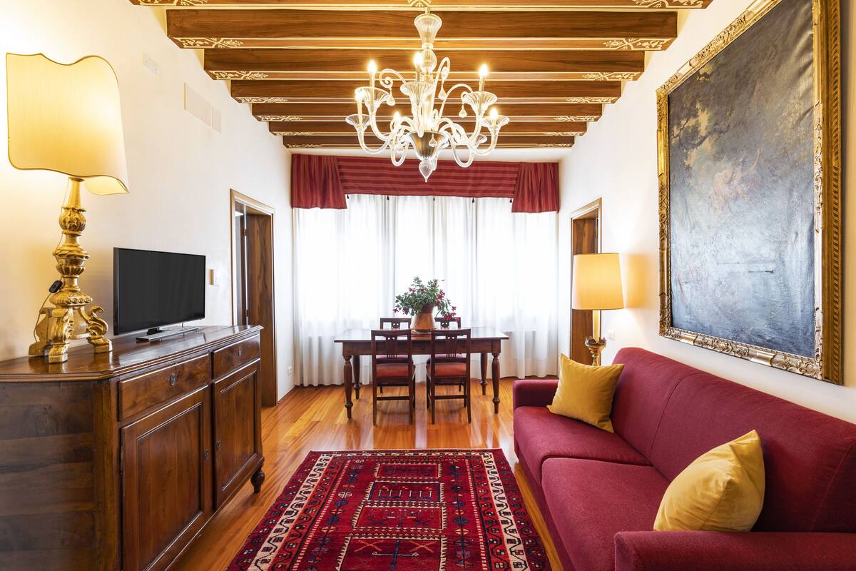 A living room with a red sofa, a wooden coffee table, a TV on a wooden cabinet, and a chandelier.