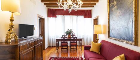 A living room with a red sofa, a wooden coffee table, a TV on a wooden cabinet, and a chandelier.