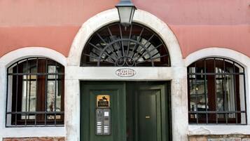Un edificio con puerta verde, fachada de ladrillo y ventana con reja metálica.