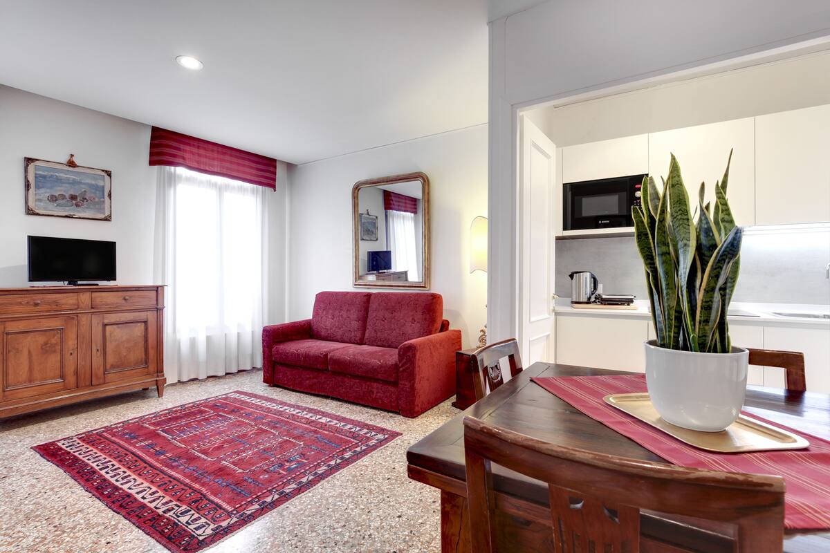 A living room with a red sofa, wooden cabinet, flat-screen TV, and a red rug.
