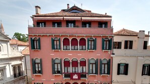 A multi-story building with a pink facade, green shutters, and a tiled roof.