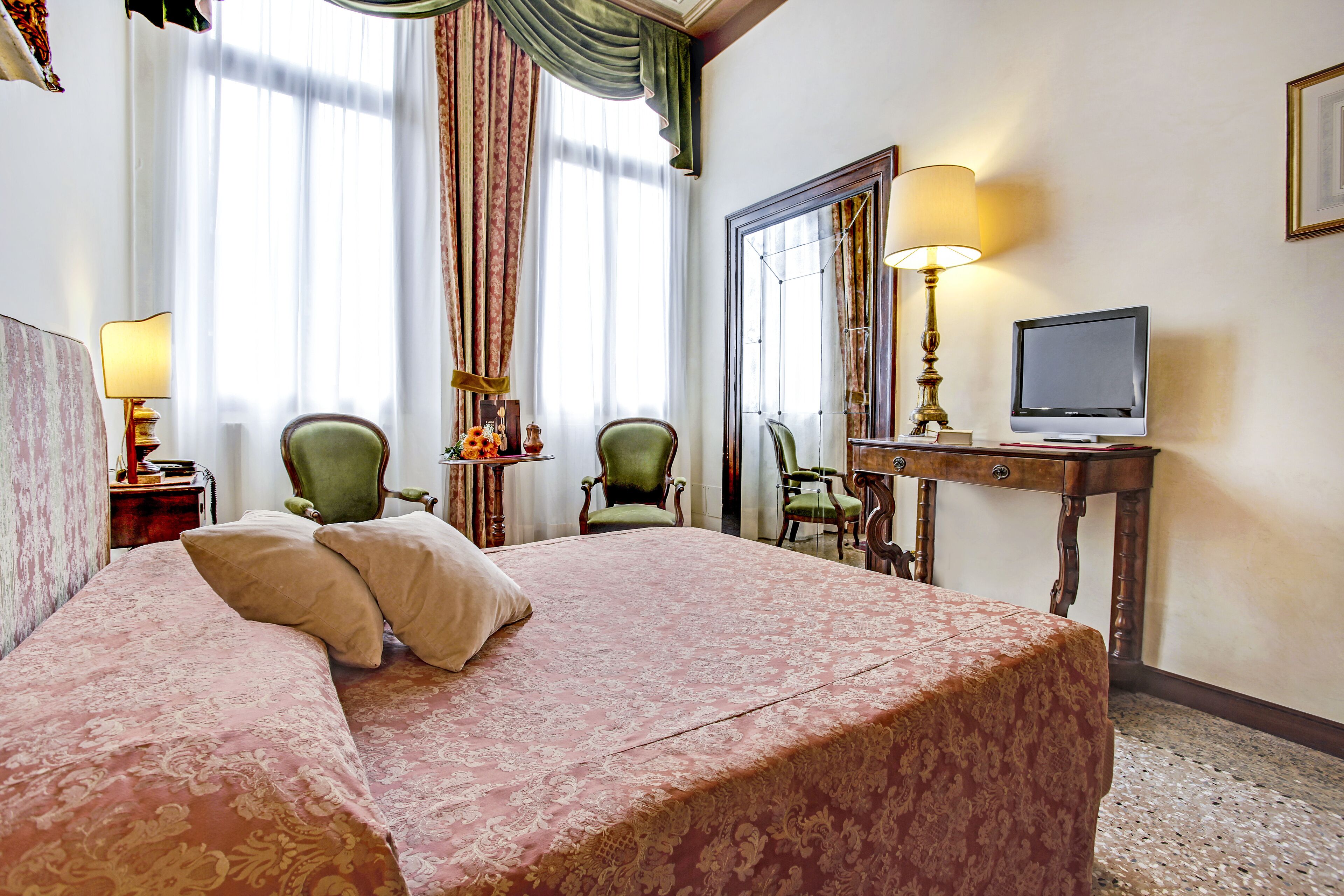 A hotel room with a large bed, two chairs, a desk with a television, and a mirror.