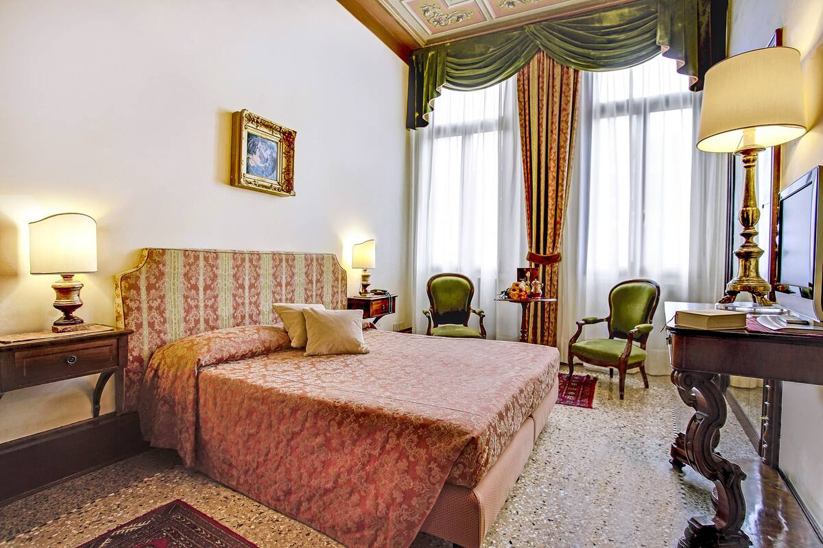 A hotel room with a large bed, two chairs, a desk, and a lamp.