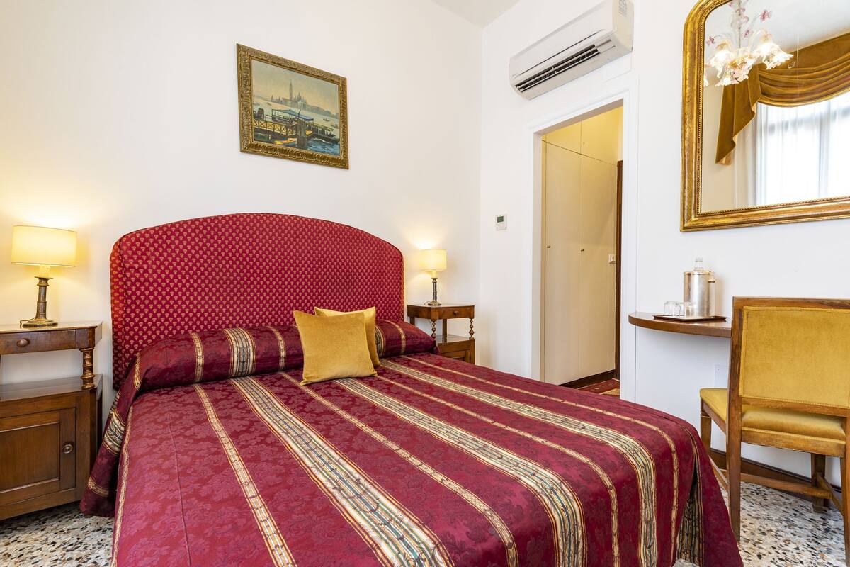 A hotel room with a large bed, two bedside tables, a chair, a mirror, and a painting on the wall.