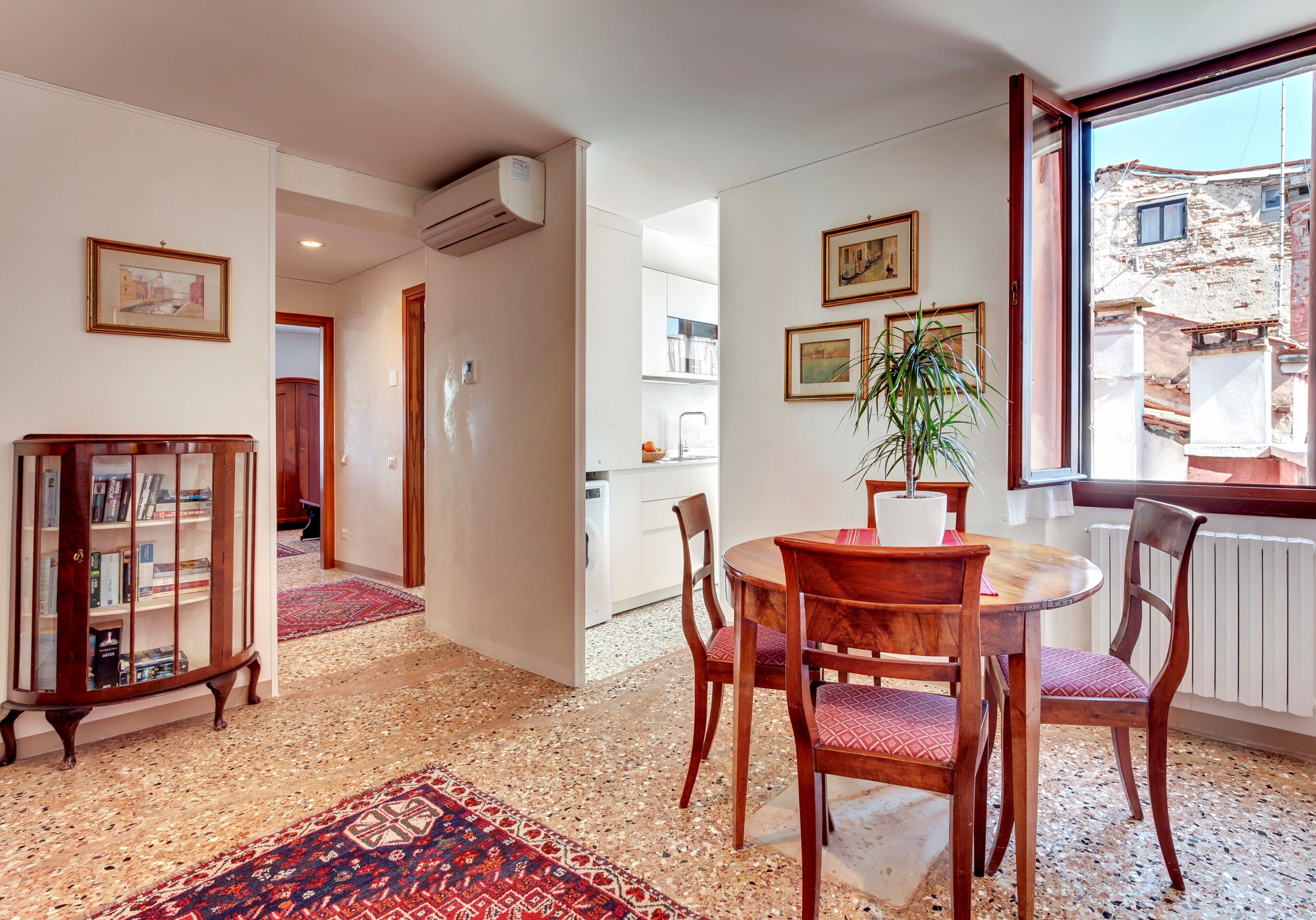 A dining area with a round wooden table, four chairs, and a red patterned rug.