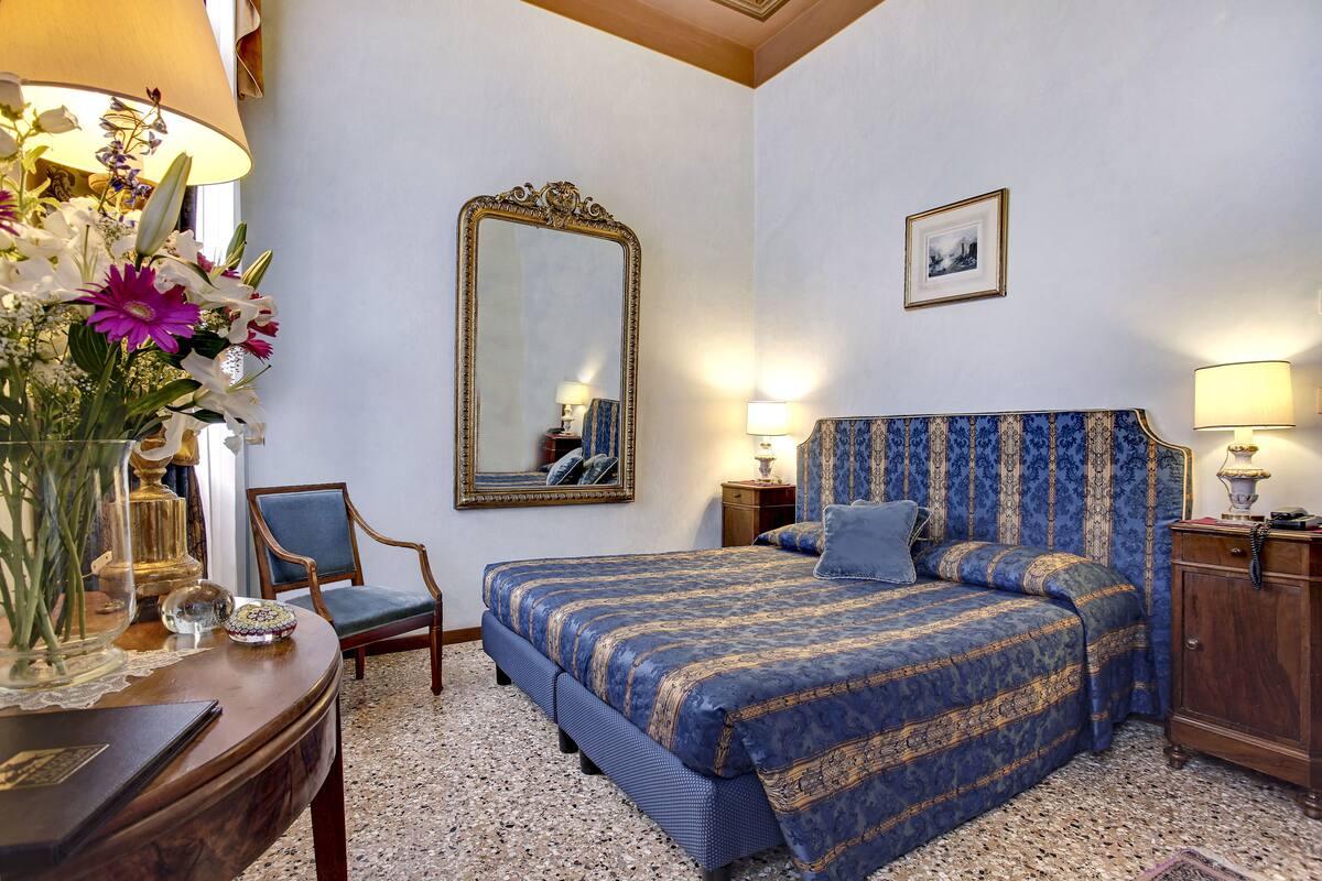 A bedroom with a large bed, a chair, a dresser, a mirror, and a vase of flowers.
