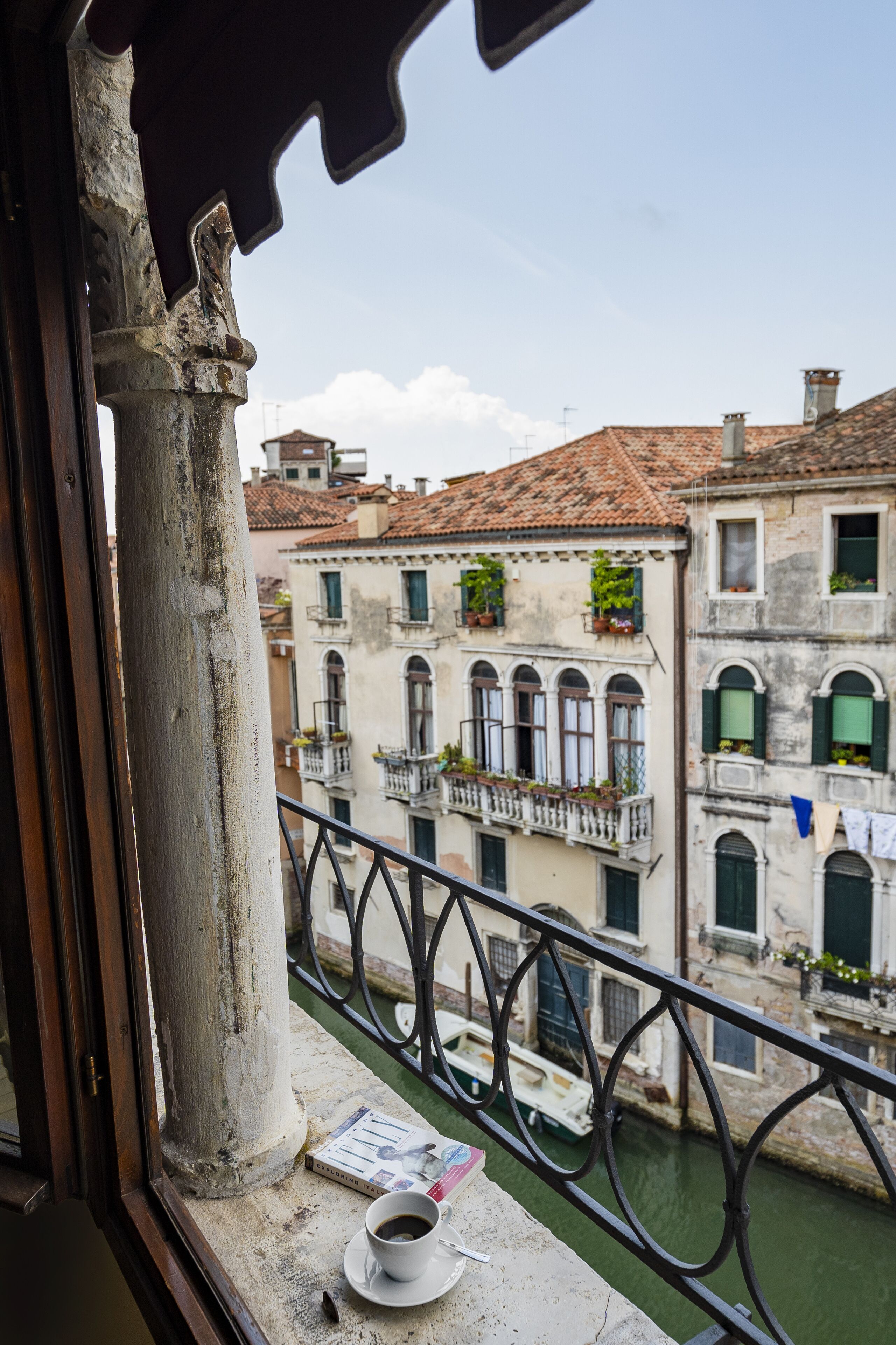 A balcony with a view of a canal, a white cup on the windowsill, and a newspaper.