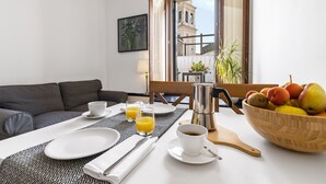 A breakfast setup with a table, plates, cups, a bowl of fruit, and a coffee maker.