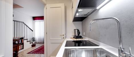A modern kitchen with stainless steel appliances, a built-in sink, and a red rug leading to a staircase.