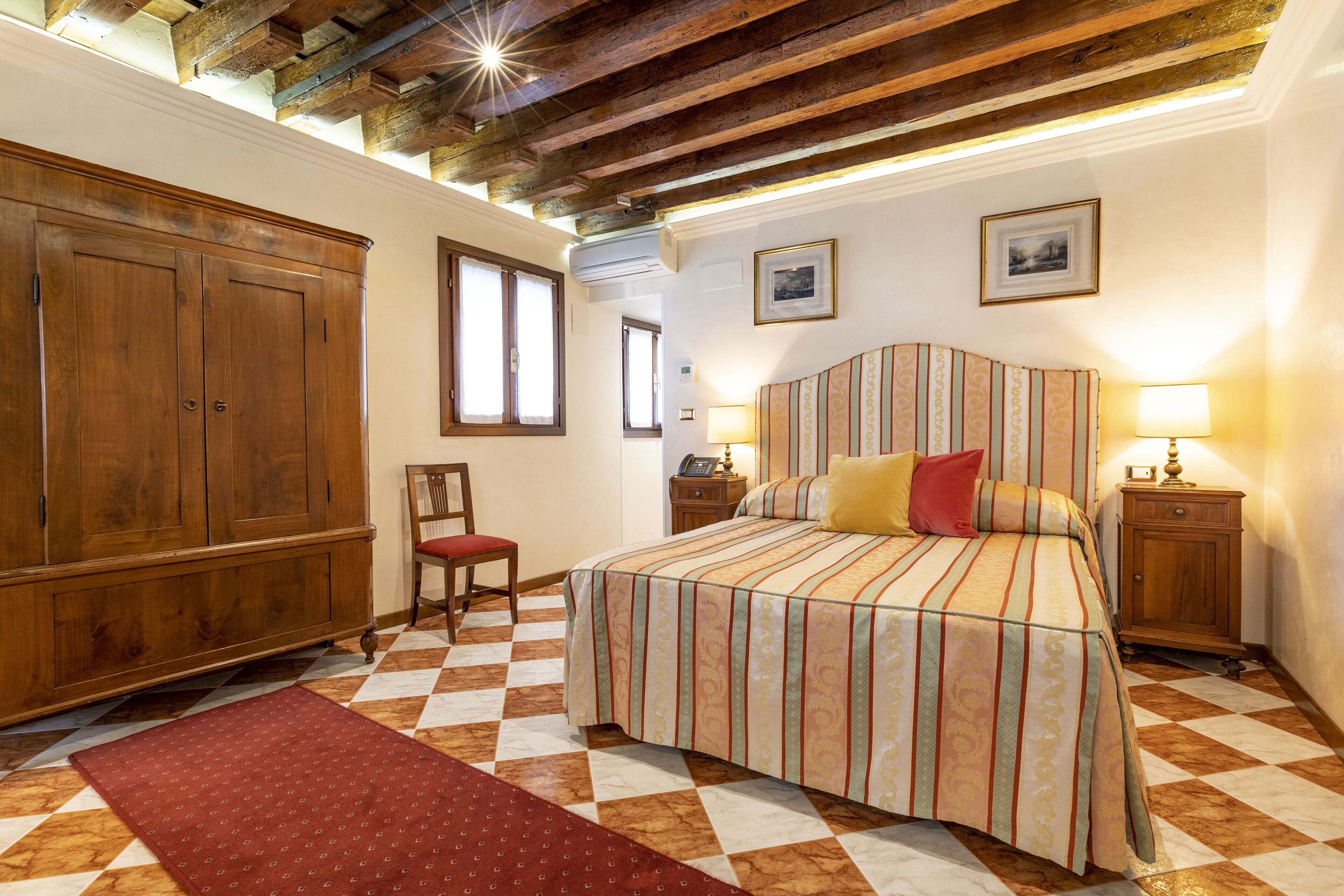 Une chambre avec un sol à carreaux, un lit avec une literie à rayures, des meubles en bois et des tableaux encadrés accrochés au mur.