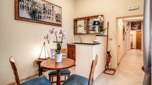 Ein Essbereich mit einem runden Tisch, Stühlen und einem Blumenstrauß. Im Hintergrund ist eine Küche mit Spüle und Schränken zu sehen.